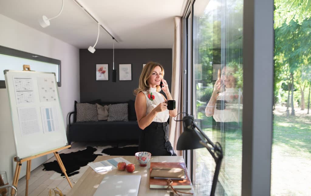 Mature woman working indoors in home office in container house in backyard.